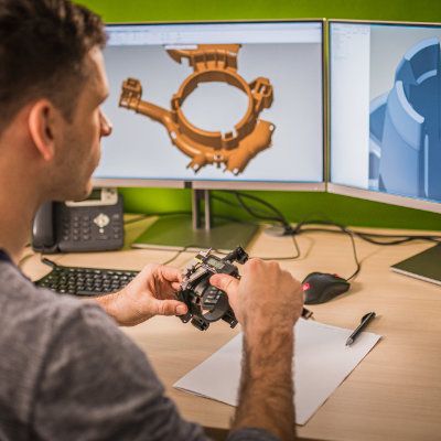 Engineer comparing a 3D CAD model on screen with a physical prototype in hand